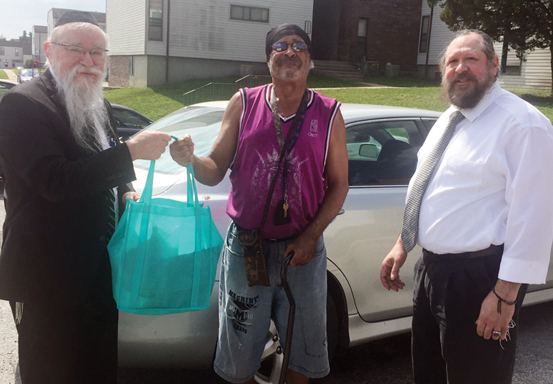 Rabbi Benzion Friedman (left) and Scott Winokur (right) deliver meals to Michael, a client of Kansas City Kosher Meals on Wheels